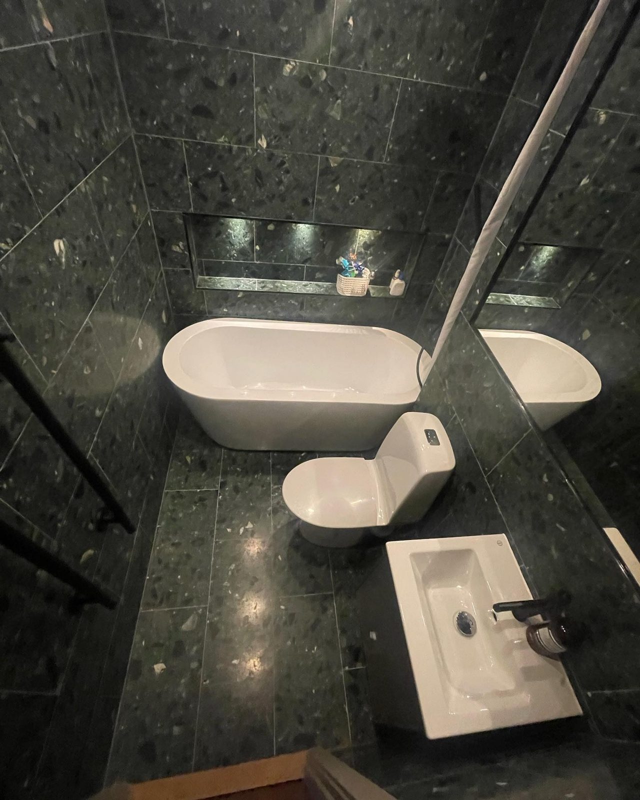 Renoverat badrum med mörkgrön terrazzo, fristående badkar och belyst nisch